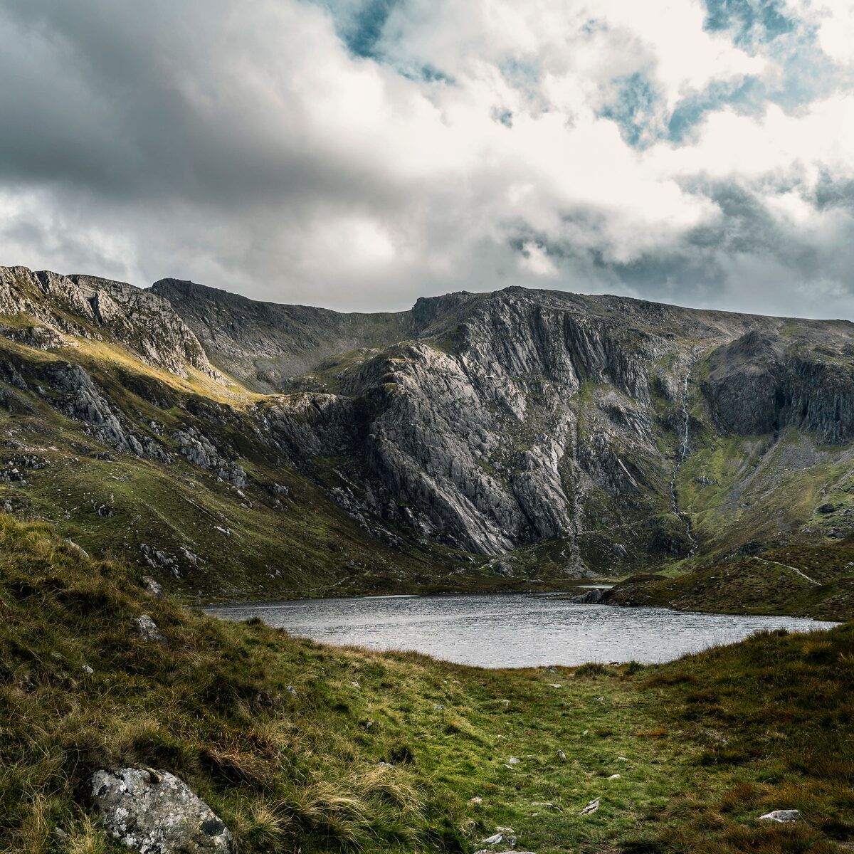 A quiet mountain tarn beneath cloud-covered cliffs in Snowdonia
